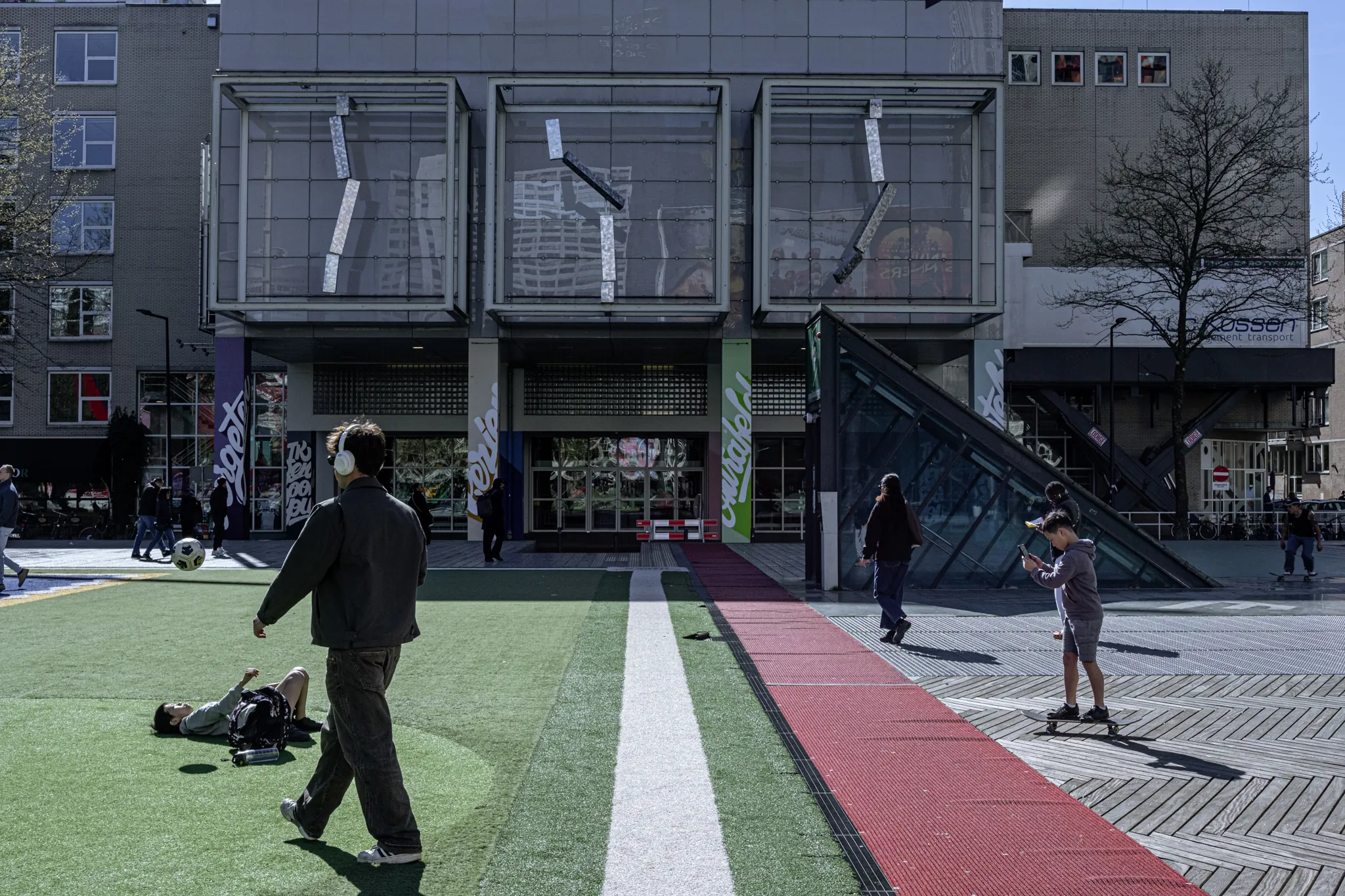 Street photography in the Netherlands Rotterdam schouwburgplein layer image including skaters and a boy trowing a ball in the air.