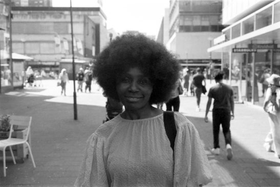 Woman posing in front of bessa r3a 35mm film trix400 without flash.